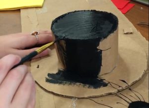 Painting cardboard hat black with paint brush