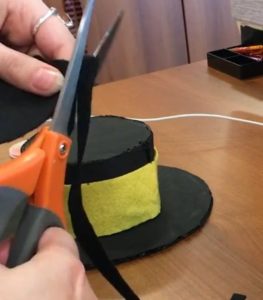 Using scissors to cut black felt into straps for the hat