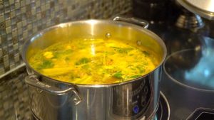 Large stock pot filled with bone broth on a stove top while beginning to boil
