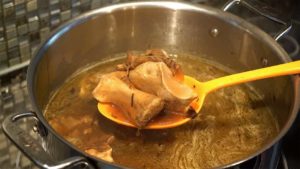 Large stock pot on marble counter-top with cooked beef bones scooped in a large spoon