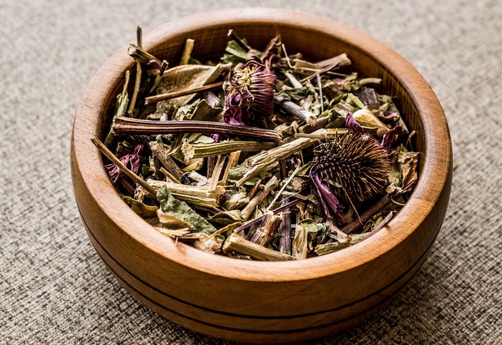 Dried echinacea flowers, stems, leaves, and roots, in a wooden bowl.