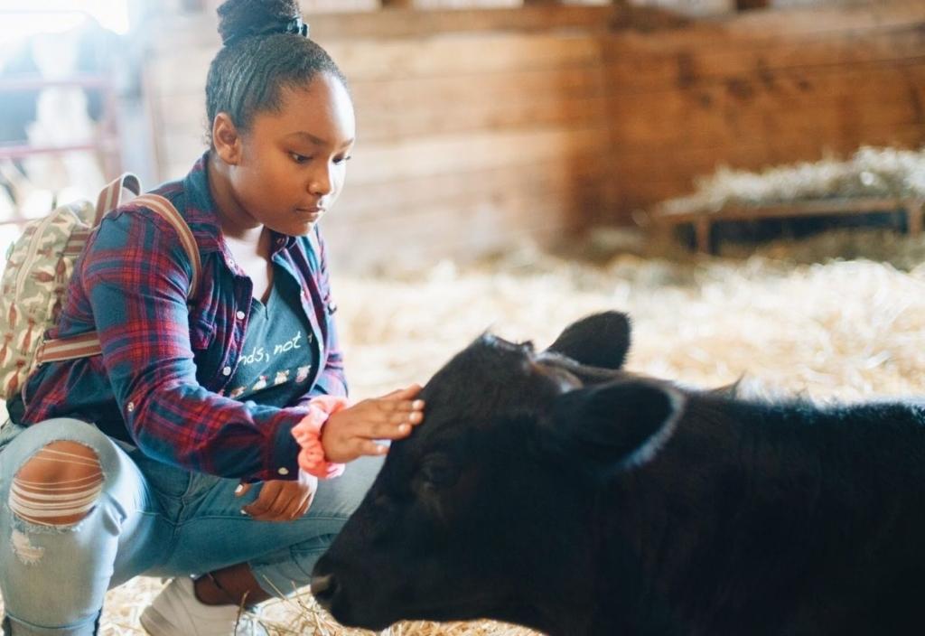 Genesis Butler squatting down to pet a cow that is laying down. Happy International Women's Day: 6 women changing the world for animals
