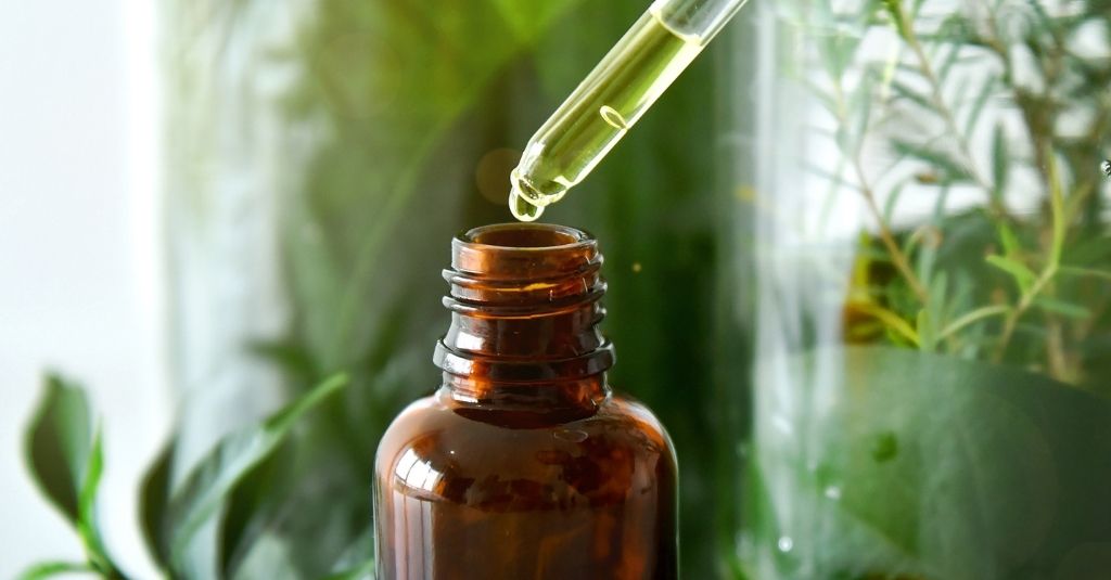 Brown glass supplement bottle and a glass dropper surrounded by greenery