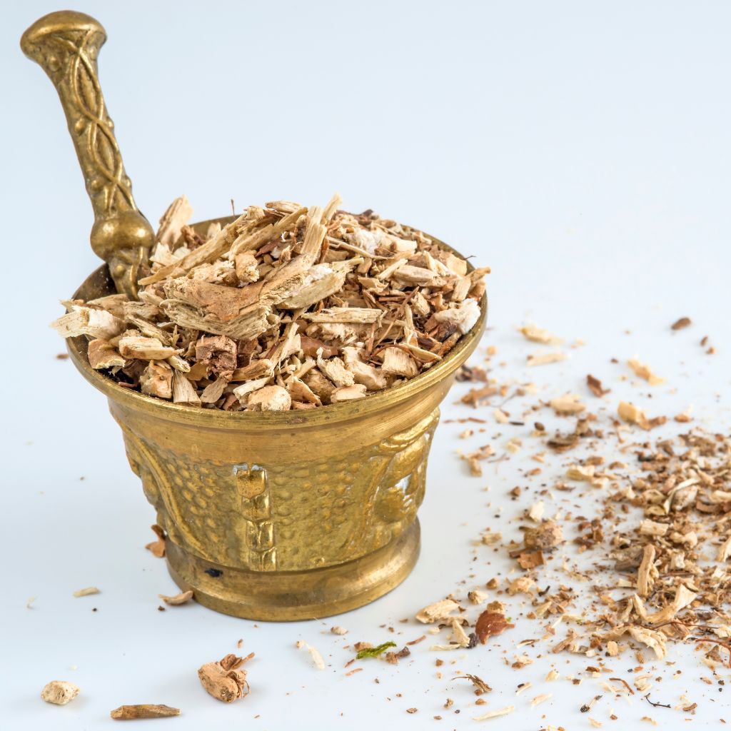 An ornate golden bucket with stirring rod containing small pieces of dried hydrangea root. 