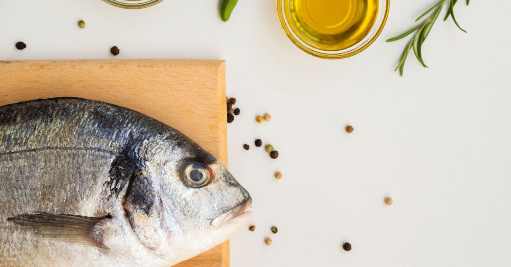 Photo of a table top with a fish on a cutting board to illustrate a blog about the benefits of Cod Liver Oil, Sardines and Anchovies for Dogs & Cats.
