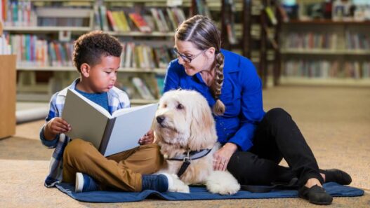 A dog in a library reading with a child and woman.