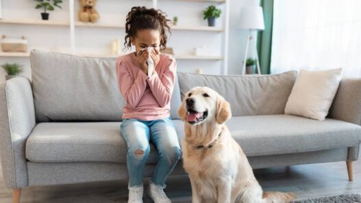 A sick girl sits on a couch with a dog nearby.