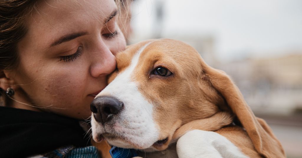 A woman kissing a dog to show bonding with pets.