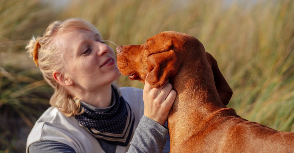 A human woman crouched down to bond with a dog.